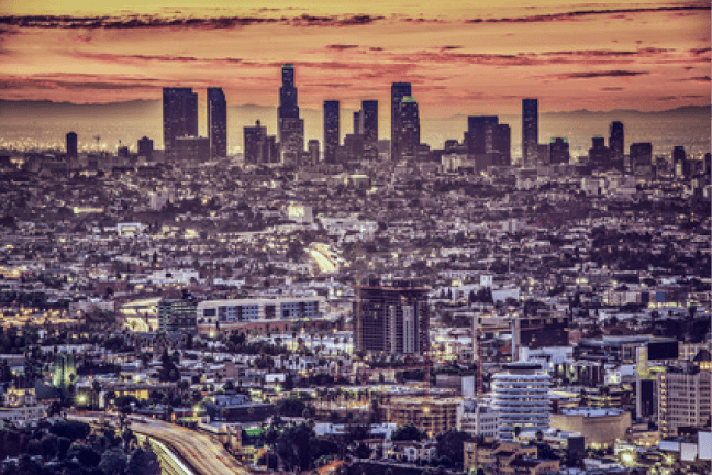 Stadtansicht von Los Angeles bei Sonnenuntergang mit Silhouette der Skyline und urbaner Landschaft.